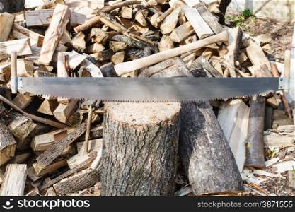 two-handled saw and ax in chopping block, pile of firewood on rustic courtyard