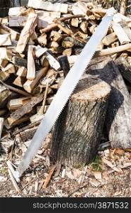 two-handled saw and ax in deck for chopping firewood, pile of wood on rustic courtyard