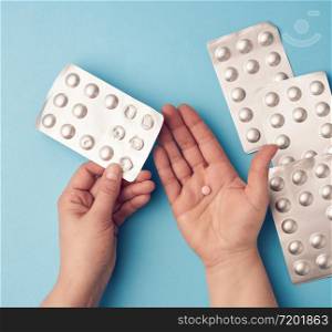 two hands hold a package of round tablets in blister packs, blue background, top view
