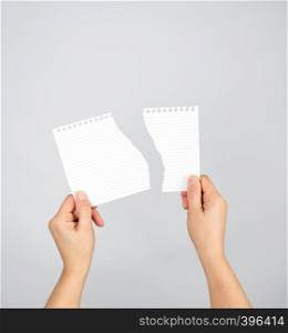 two hands hold a torn piece of paper on a gray background, copy space