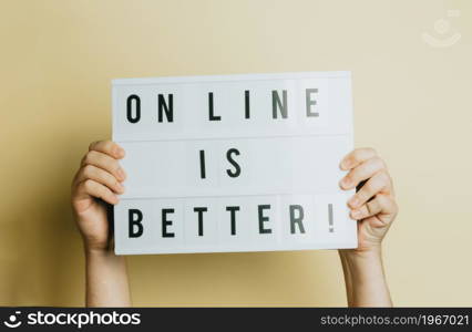 Two hands holding a sign that says online is better over a pastel yellow background, styling and design concept, copy space, buy online and e-commerce