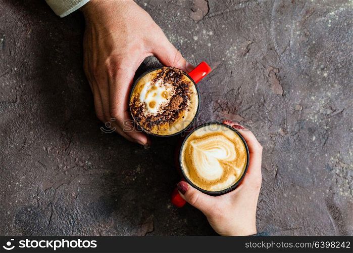 Two hands holding cups of hot coffee on dark background, top view. Morning coffee for couple in love