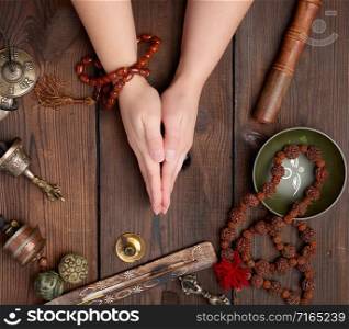 two hands in a prayer pose on a wooden brown table in the middle of vintage Tibetan meditation tools, alternative medicine, top view