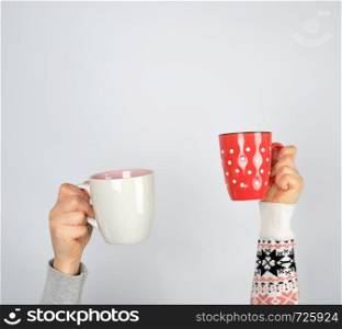 two hands in a sweater holding ceramic mugs on a white background, copy space