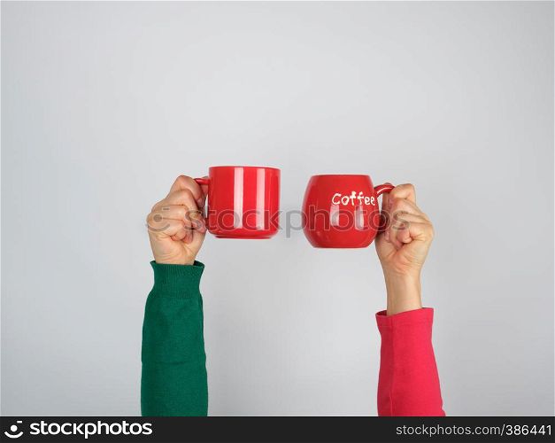 two hands in a sweater holding red ceramic mugs on a white background