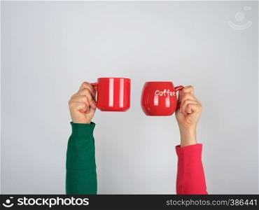 two hands in a sweater holding red ceramic mugs on a white background