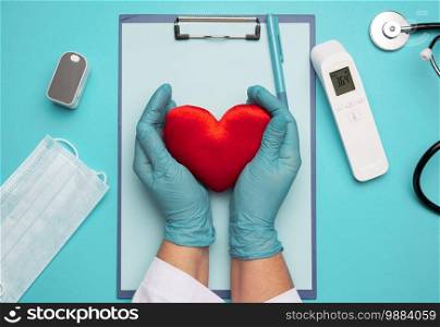 two hands in blue latex gloves holding a red textile heart, donation concept, close up