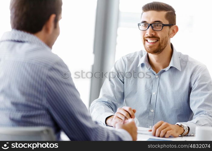 Two handsome businessmen in office. Two handsome businessman in office sitting at desk and talking