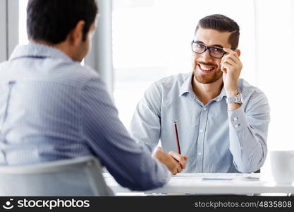 Two handsome businessmen in office. Two handsome businessman in office sitting at desk and talking