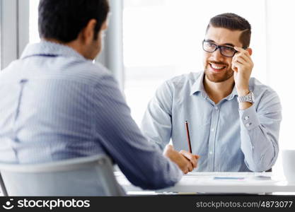 Two handsome businessmen in office. Two handsome businessman in office sitting at desk and talking