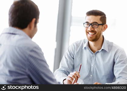 Two handsome businessmen in office. Two handsome businessman in office sitting at desk and talking