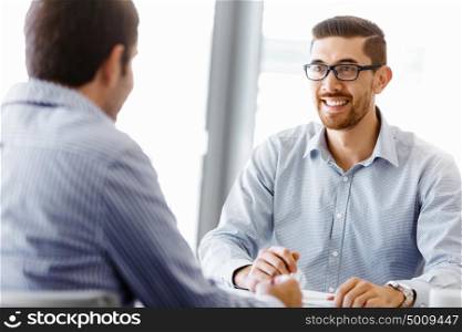 Two handsome businessmen in office. Two handsome businessman in office sitting at desk and talking