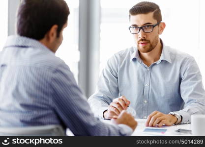 Two handsome businessmen in office. Two handsome businessman in office sitting at desk and talking