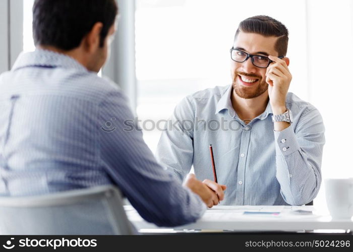 Two handsome businessmen in office. Two handsome businessman in office sitting at desk and talking