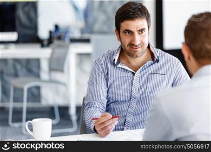 Two handsome businessmen in office. Two handsome businessman in office sitting at desk and talking