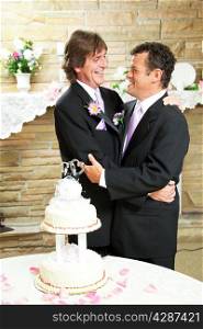 Two handsome gay men in tuxedos embrace with love at their wedding reception. Wedding cake and rose petals in foreground.