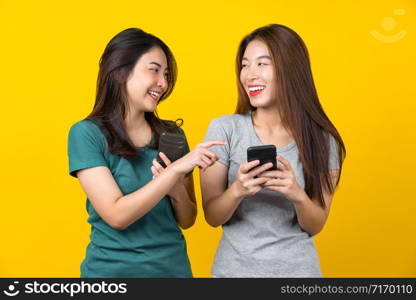 Two Happiness Asian smiling young woman gamer using smart mobile phone and playing games on isolated yellow color background, Lifestyle and leisure with hobby concept