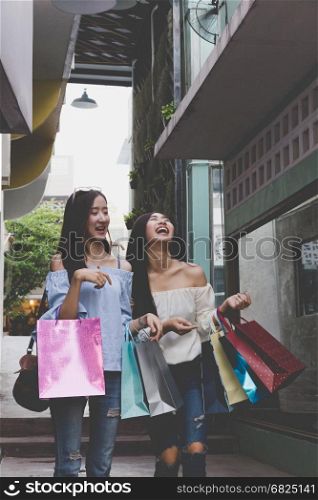 two happy asian shopaholic women with colorful shopping bags at department store shopping mall