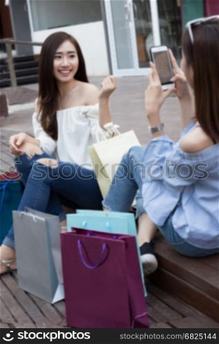 two happy asian shopaholic women with colorful shopping bags take photo at department store shopping mall, blur background