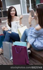 two happy asian shopaholic women with colorful shopping bags take photo at department store shopping mall, blur background
