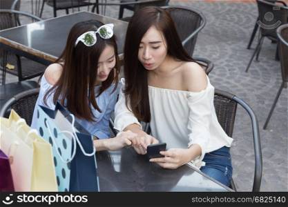 two happy asian shopaholic women with smartphone and colorful shopping bags at cafe coffee shop restaurant