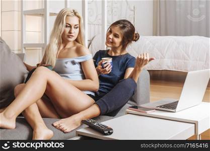 Two happy beautiful women in a relationship relaxing at home drinking coffee together.