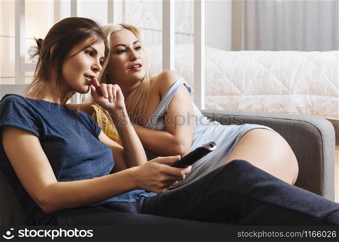 Two happy beautiful women in a relationship watching television together.
