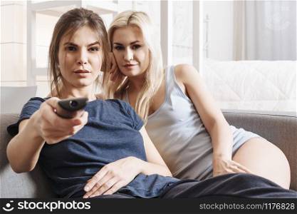 Two happy beautiful women in a relationship watching television together.