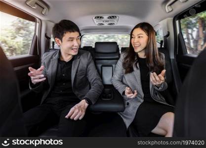 two happy business man and woman talking while sitting at the back seat of a car