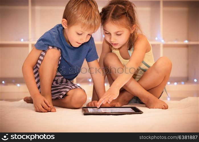Two happy children playing on the tablet in the child&rsquo;s room at home, best friends with pleasure spending time together, smart kids using smart technology