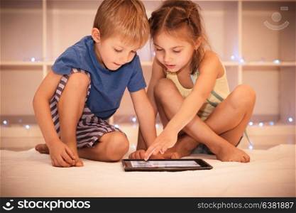 Two happy children playing on the tablet in the child&rsquo;s room at home, best friends with pleasure spending time together, smart kids using smart technology