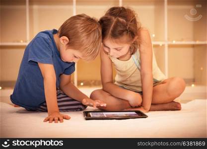 Two happy children playing on the tablet in the kids room at home, best friends with pleasure spending time together, smart kids using smart technology