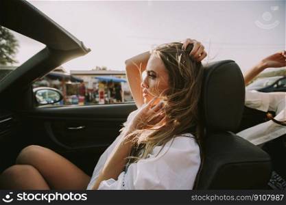 Two happy female friends driving in white cabriolet car and looking for freedom and fun