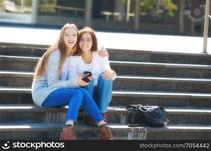 Two Happy Female Teenagers Talking Together in the Street, Sitting on the Stairs