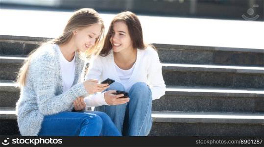 Two Happy Female Teenagers Talking Together in the Street with Mobil Phones, Sitting on the Stairs