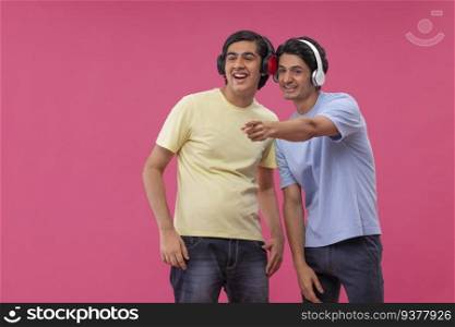 Two happy friends listening to music against pink background