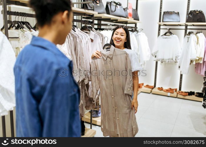 Two happy girls choosing clothes in clothing store. Women shopping in fashion boutique, shopaholics, shoppers looking garment on hangers. Two happy girls choosing clothes in clothing store