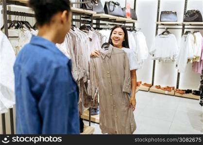 Two happy girls choosing clothes in clothing store. Women shopping in fashion boutique, shopaholics, shoppers looking garment on hangers. Two happy girls choosing clothes in clothing store