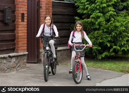Two happy girls in school uniform riding to school on bicycles
