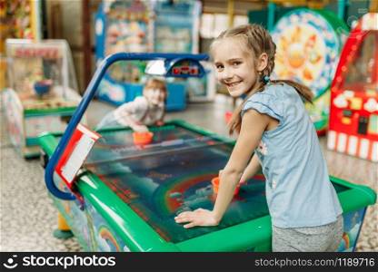 Two happy girls plays air hockey in children game center. Excited childs having fun on playground indoors. Kids playing on machine in amusement centre. Two happy girls plays air hockey in game center