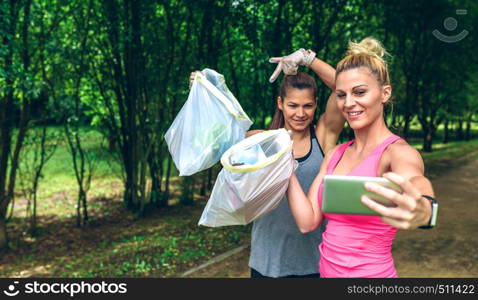 Two happy girls taking a selfie showing trash bags after plogging. Two girls taking a selfie after plogging