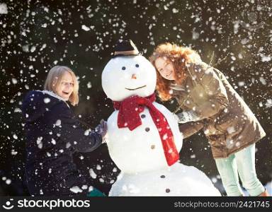 Two happy pretty girls enjoying building a snowman on a snowy winter day