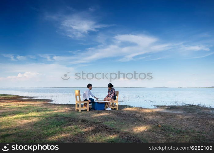 Two happy siblings playing a game with chess near the lake in nature. children playing a game with chess