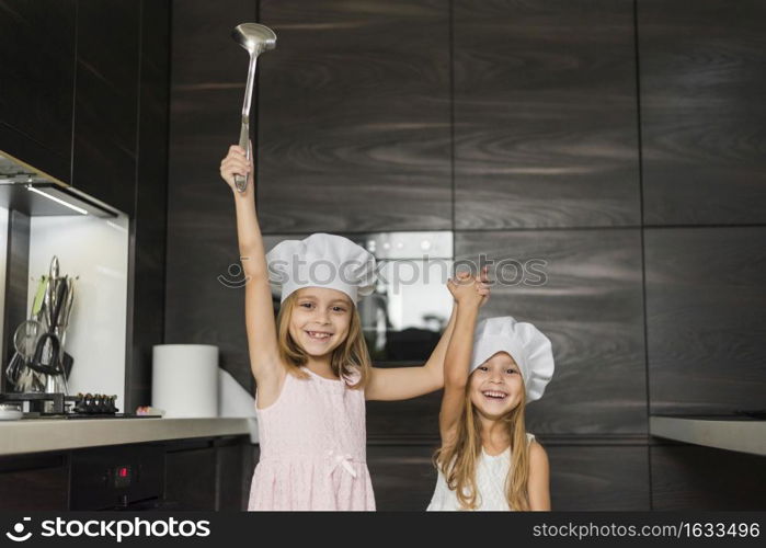 two happy sisters wearing chef hat kitchen holding their hands