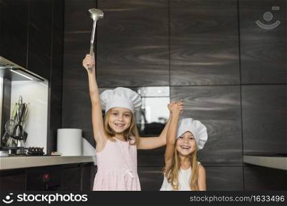 two happy sisters wearing chef hat kitchen holding their hands