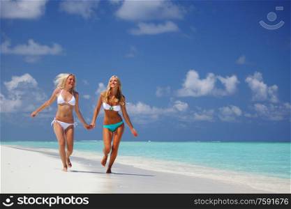 Two happy smiling girls female friends run along ocean coast beach holding hands, vacation at Maldives. Two girls run along ocean beach
