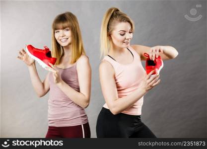 Two happy sporty smiling women presenting sportswear trainers red shoes, comfortable footwear perfect for workout and training.. Two women presenting sportswear trainers shoes