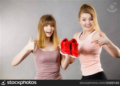 Two happy sporty smiling women presenting sportswear trainers red shoes, comfortable footwear perfect for workout and training.. Two women presenting sportswear trainers shoes