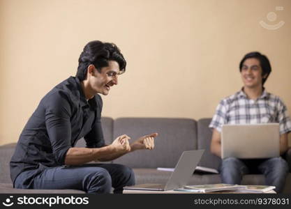 Two happy teenage boys doing homework at home using laptop