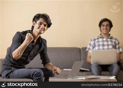 Two happy teenage boys doing homework at home using laptop